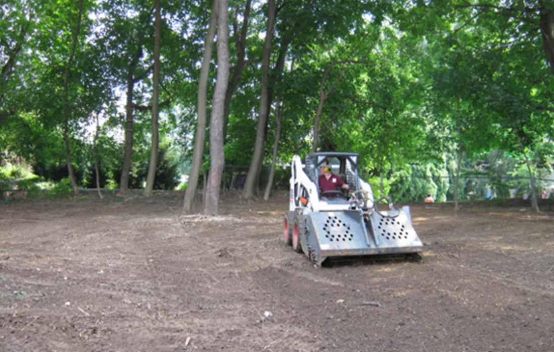 Skid steer fine-grading a wooded backyard lot