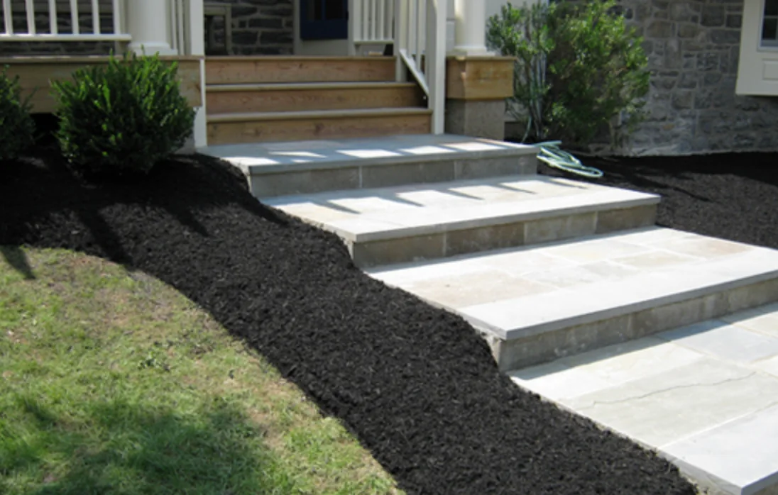 New flagstone staircase with fresh mulch beds leading to a stone home's front porch
